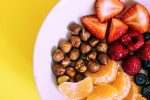 Close-up of a bowl with fresh fruits and nuts against a vibrant yellow backdrop.