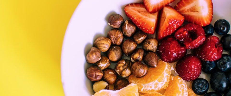 Close-up of a bowl with fresh fruits and nuts against a vibrant yellow backdrop.